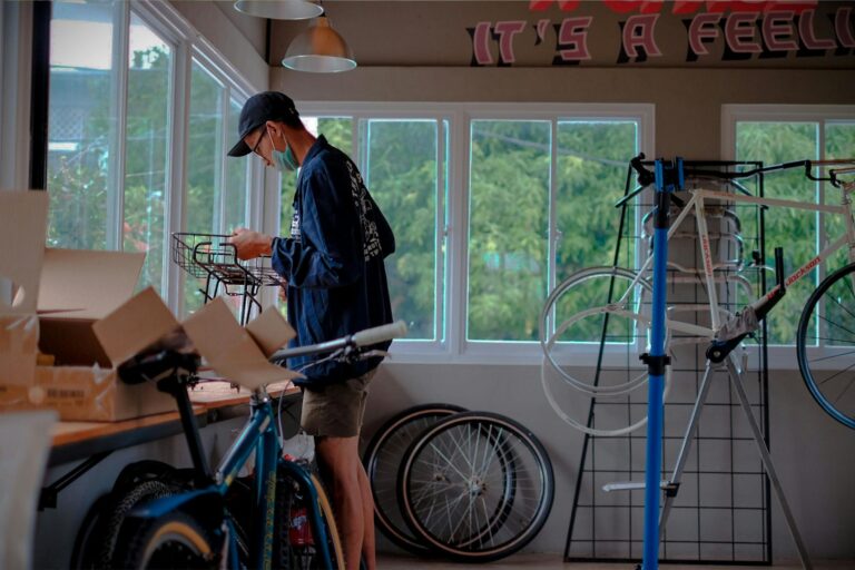 A man working on a bicycle assembly in a bright indoor workshop setting.