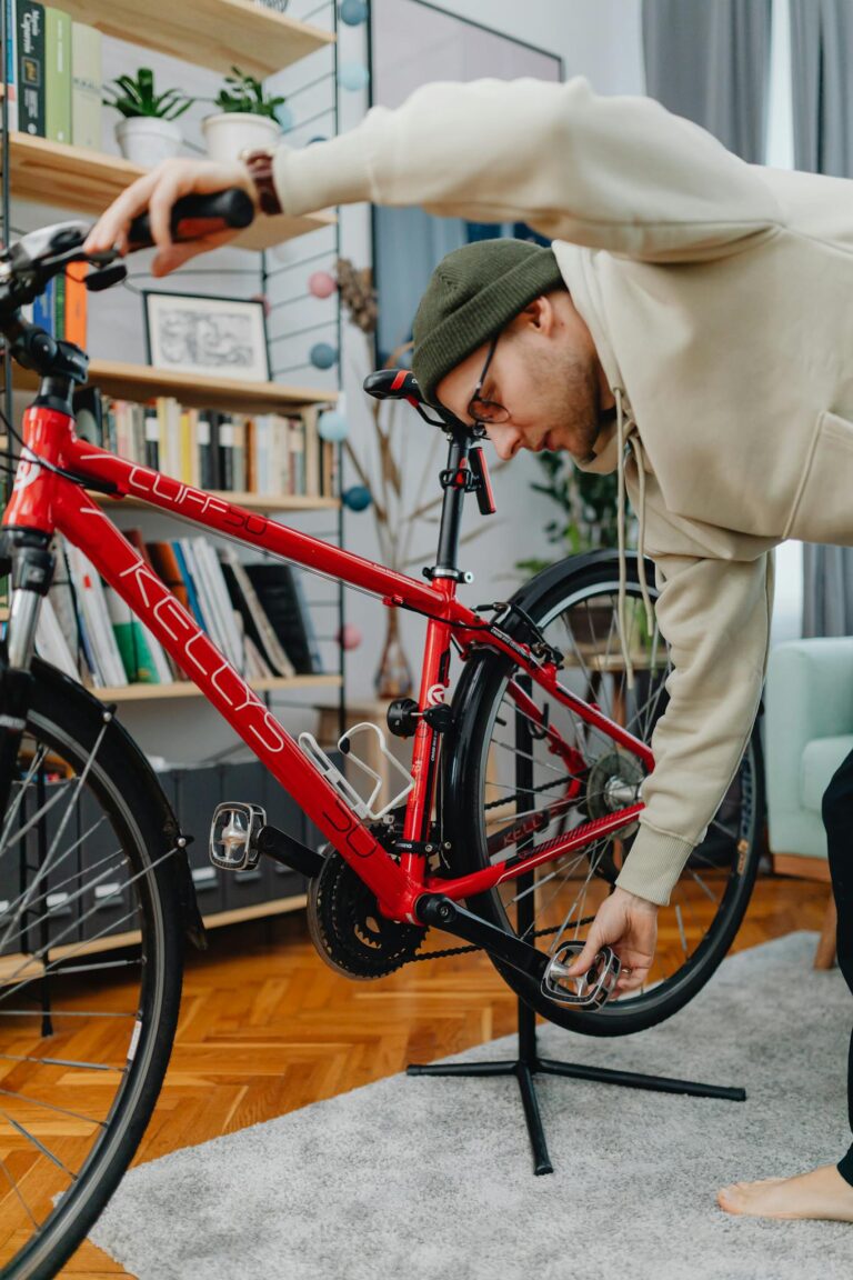 Adult male in casual wear tuning a red bicycle indoors.